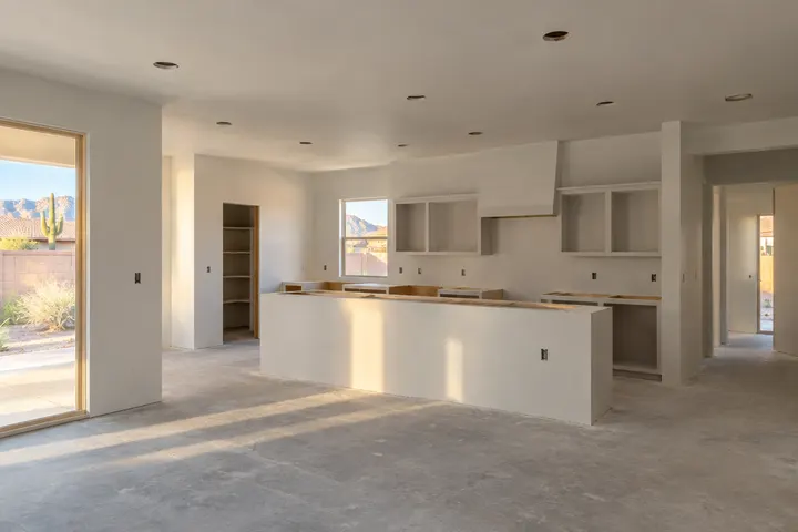 Fresh smooth drywall and primer on kitchen walls and ceiling after rough-in inspection, recessed light cutouts in the ceiling, floor still bare concrete